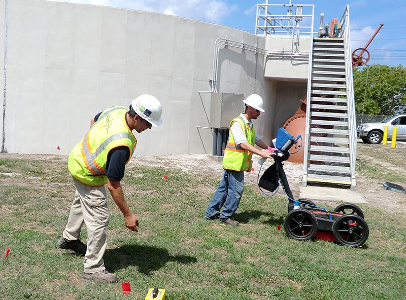Field crew using utility-locating equipment beside a building